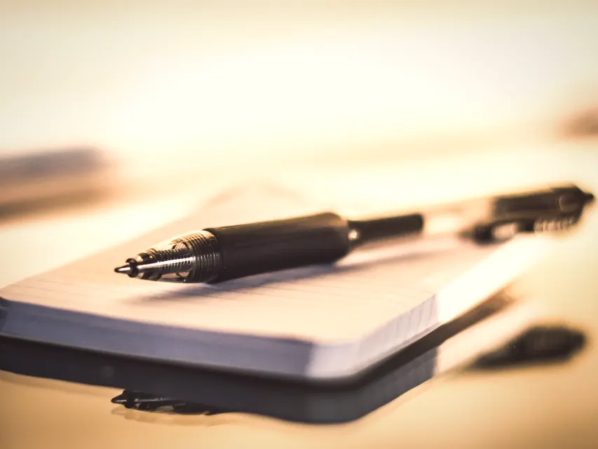 A pen resting on a closed notebook, where every project starts before any design happens